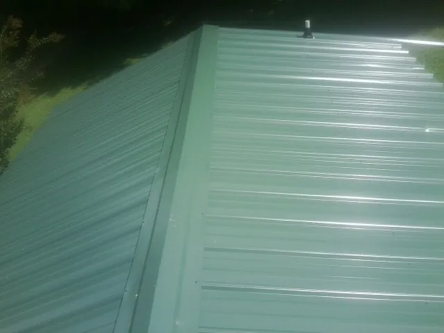 New green metal panels meeting at the ridge of a roof — Flat Roof Repair work by our crew in Otisville